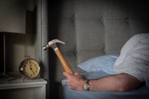 Person sleeping about to smash alarm clock with a hammer.