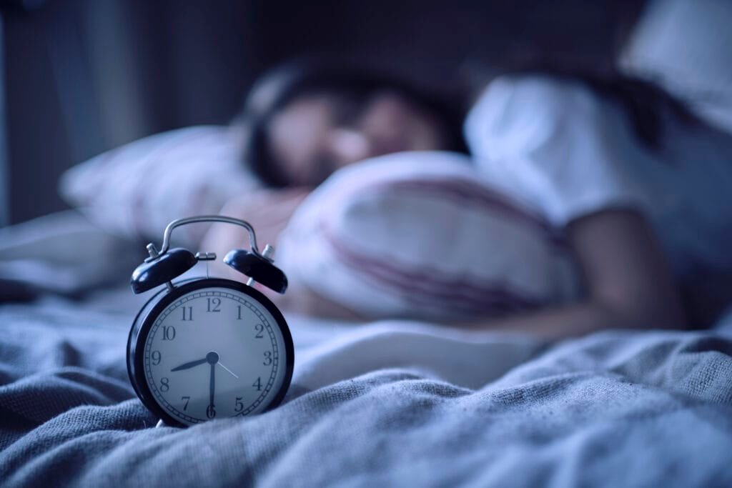 Young lady resting in her bed, midnight time shown on alarm clock, night dreams